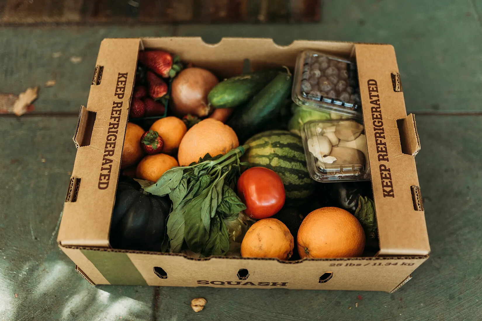 A colored photograph of a cardboard box with fruits and vegetables in it.