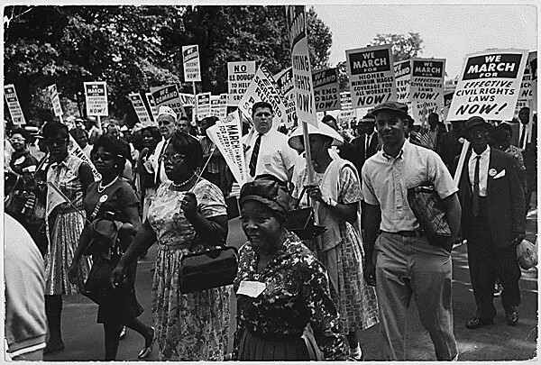 A black and white photograph of a group of people marching with signs down a road.