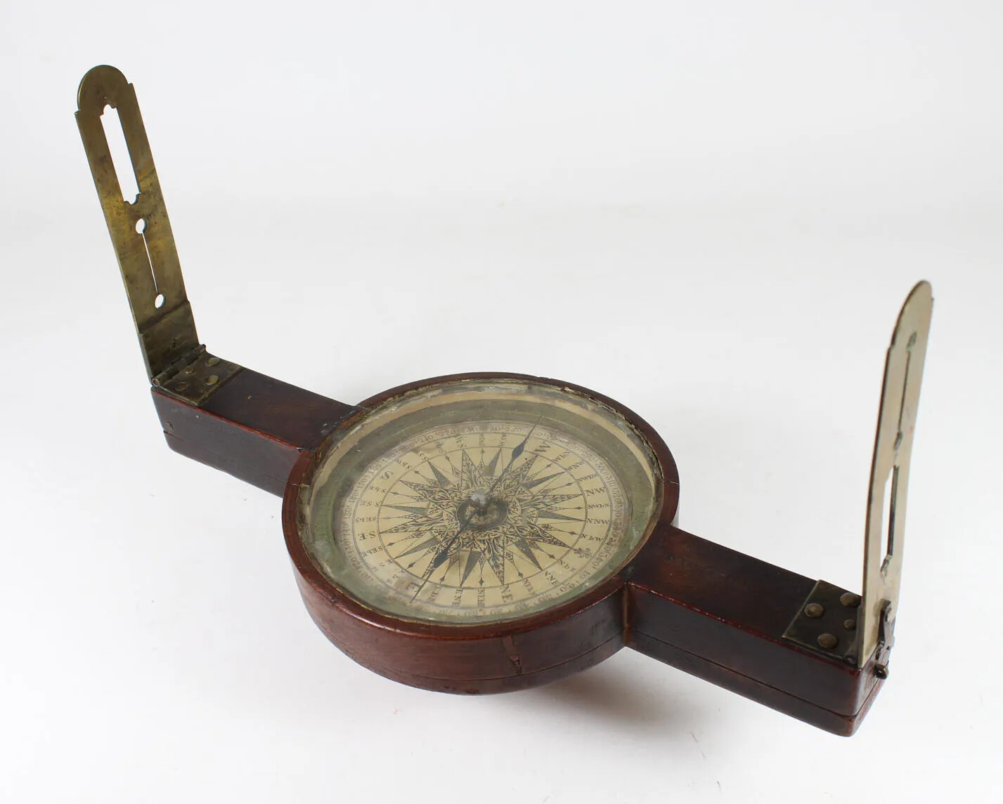 A wooden tool with a circular compass in the middle and two brass handles on either side. The handles stand up vertically, and connecting the compass and the handles are two horizontal pieces of wood.