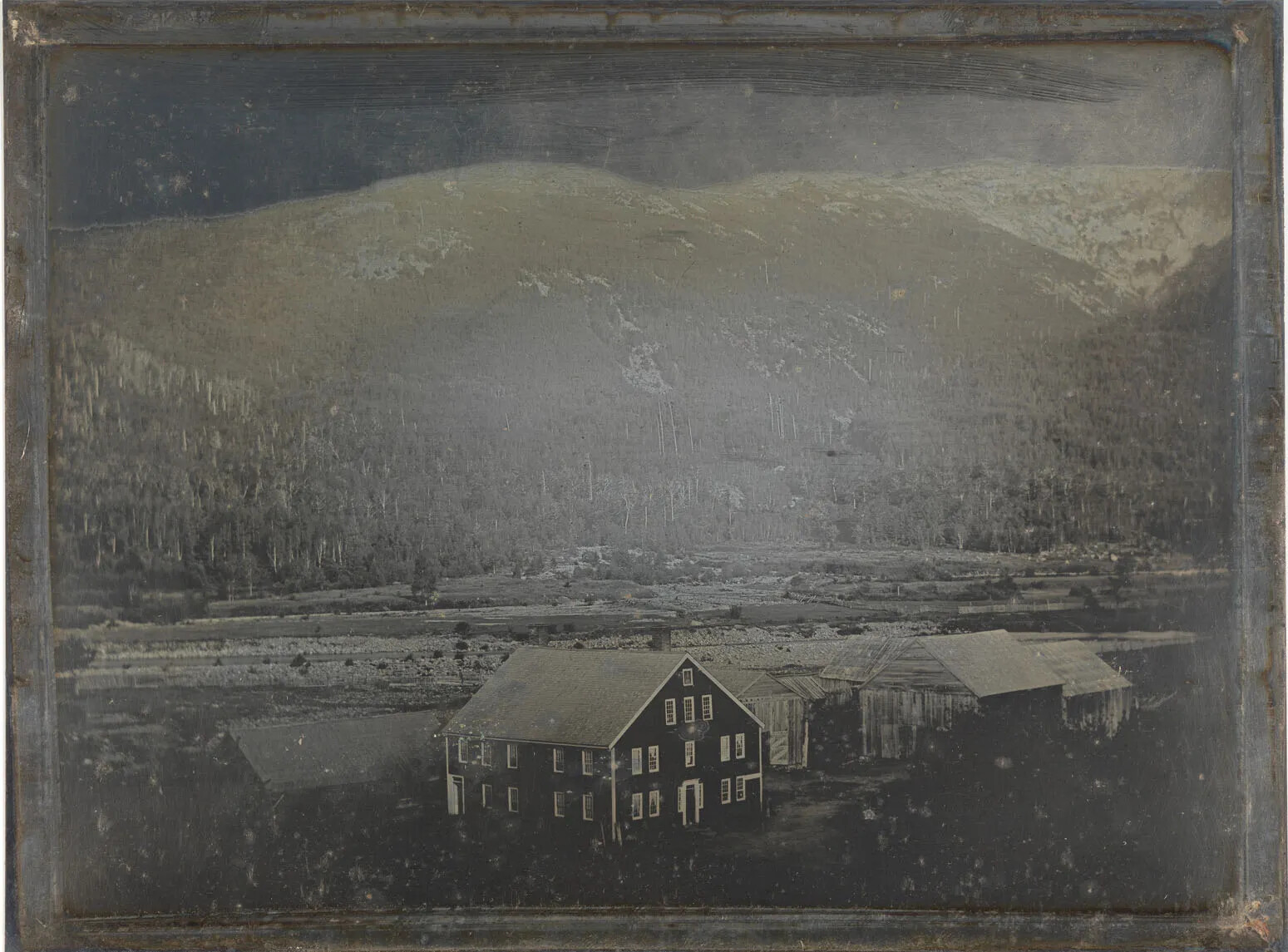 A daguerreotype of a large house and barn set in a valley of a mountain range.