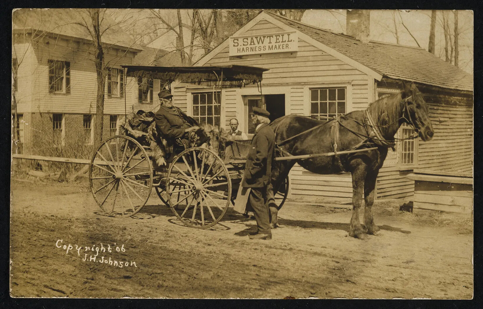 A black and white photograph of a man sitting in a horse-drawn carriage. He talks with two other men outside of a single-storied building.
