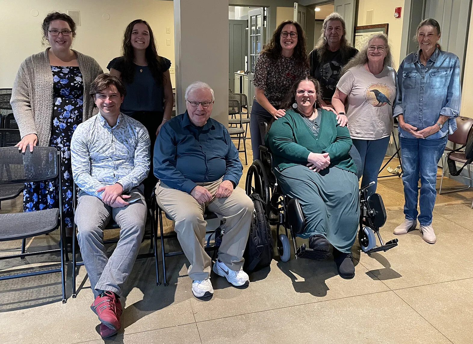 A colored photograph of a group of white men and women posed in two rows. The people in the front row are seated, and the people in the back row are standing.