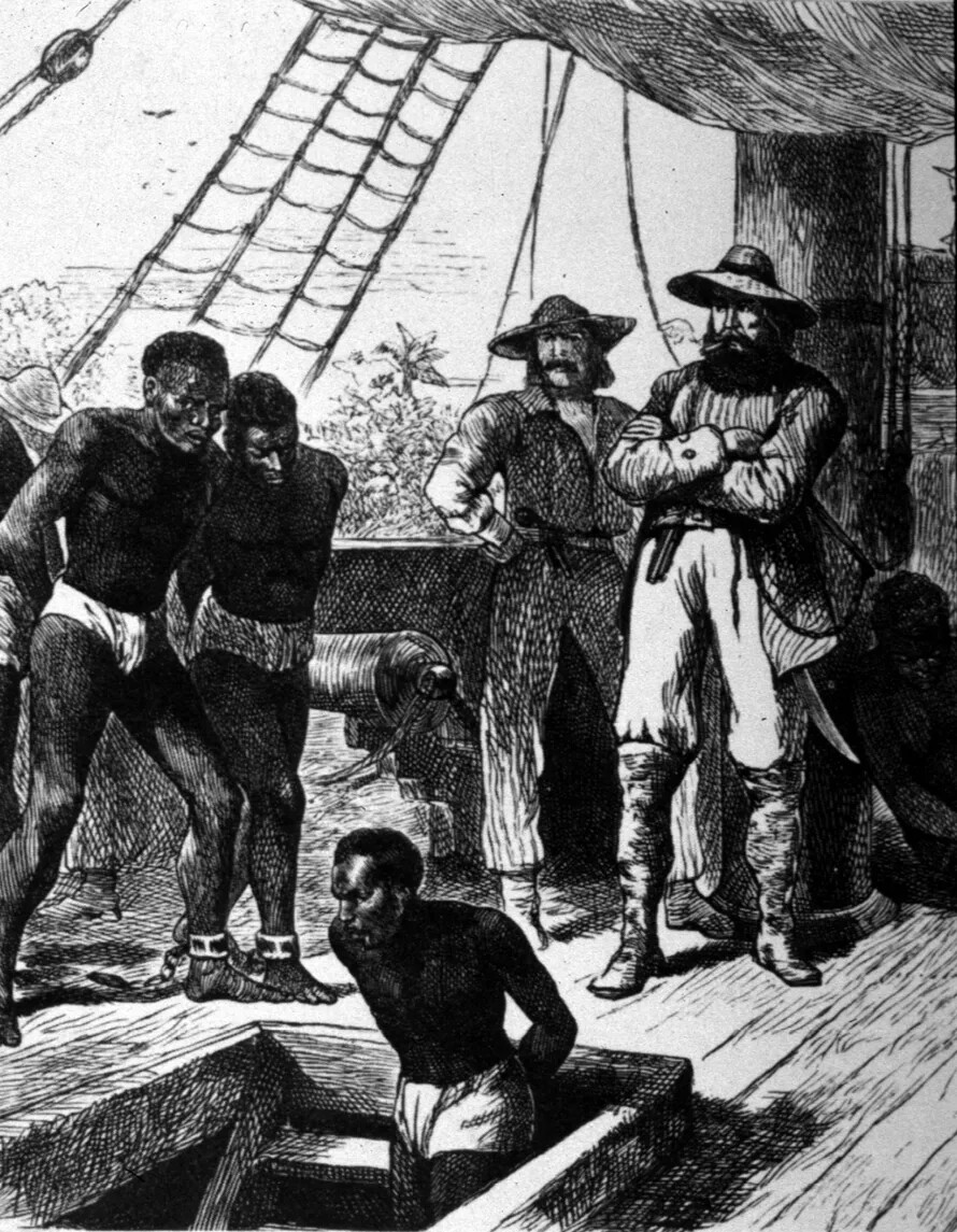 A black and white drawing of a group of Black and white men standing on the deck of a ship. The white men wear broad-rimmed hats, long-sleeved shirts and long pants. They stand off to the right and watch the group of Black men walk down a set of stairs, into the hull of the ship. The Black men wear a cloth around their waists, handcuffs, and are attached by a chain at the ankles.