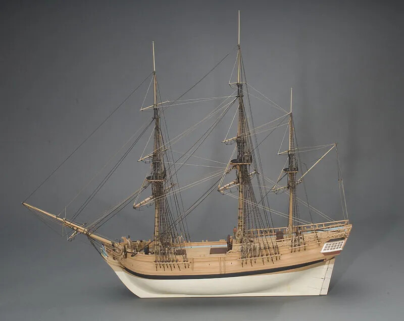 A miniature model of a ship with three tall masts. The top half of the ship's hull is colored brown and the lower half is white.