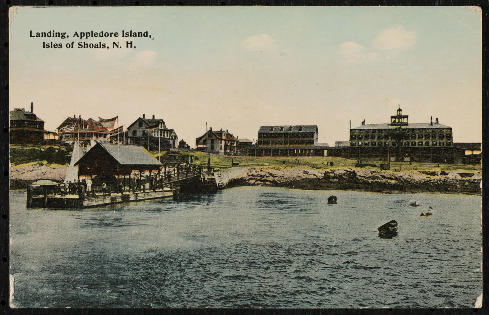 A color postcard shows a picture of water, a dock, and more than six large buildings on land in a row. The buildings are houses or hotels, and have porches. There is a sailboat docked, and people walking up the dock to the lawn and buildings. Words in the upper left read "Landing, Appledore Island, Isles of Shoals, N.H."