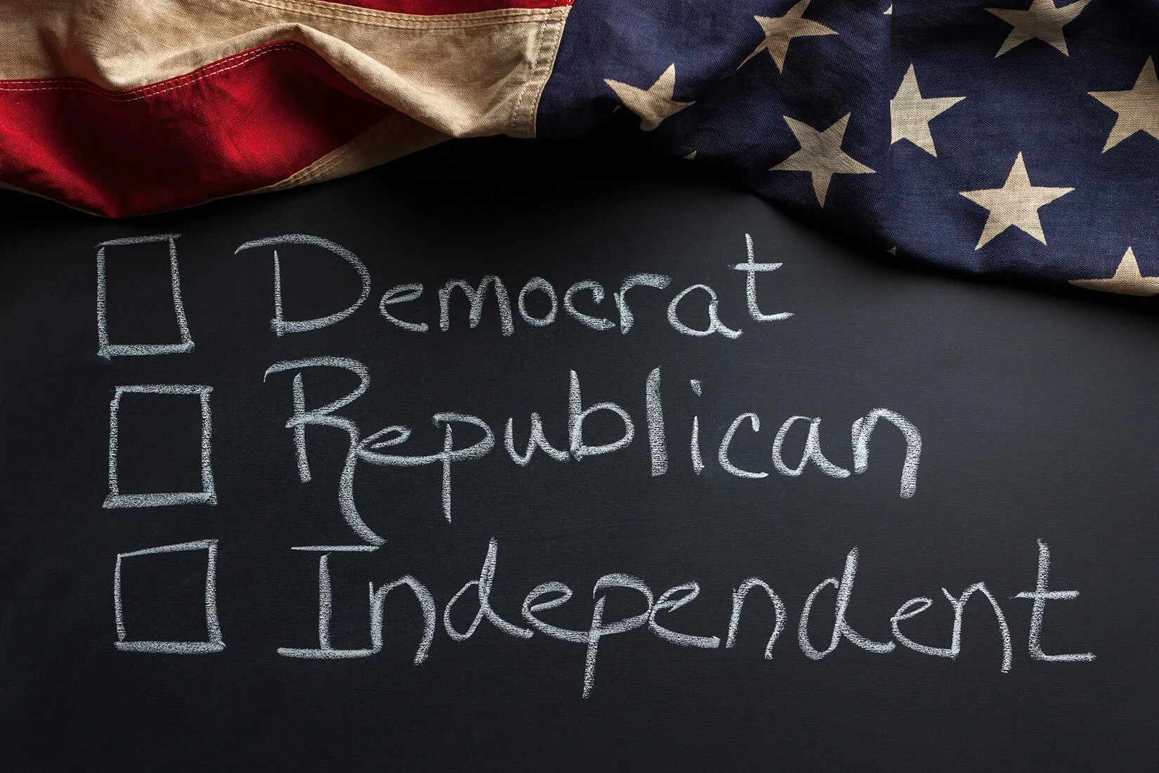 A colored photograph of a chalk board bordered in an American flag. On the chalk board are the words "Democrat," "Republican," and "Independent." Each word is handwritten in chalk and is placed next to a hand-drawn square.