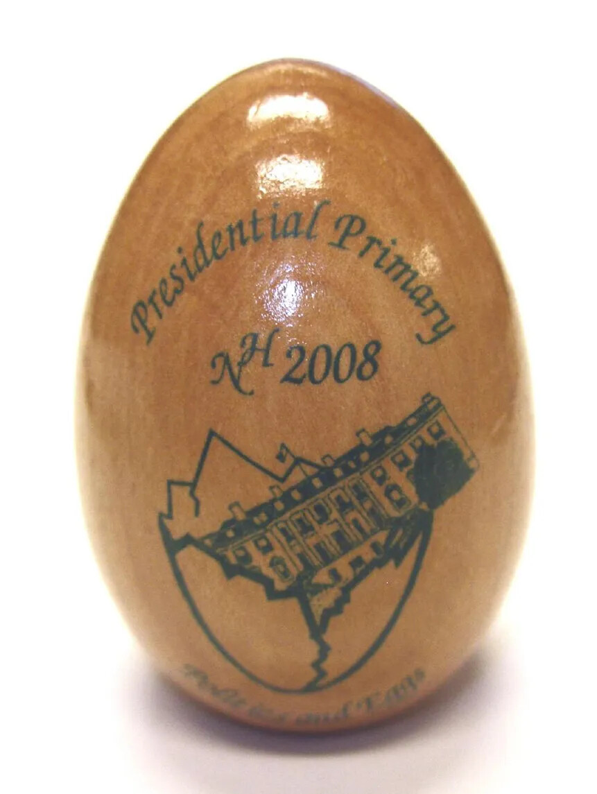 Commemorative wooden egg, imprinted in green, "Presidential Primary / NH 2008 / Politics and Eggs", with image of White House in eggshell. Birch or maple. Glossy clear finish. Flat base, 0.85" diam., to allow it to stand.