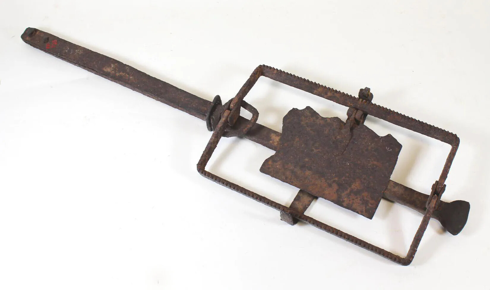A rusty metal tool, with a long handle on one end and a square base on the other, which is framed by a larger metal rectangle with jagged edges.